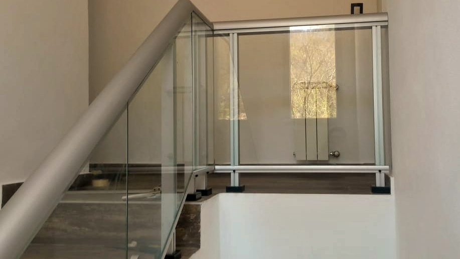 Baranda de linea Fexa, en aluminio anodizado natural y vidrios laminado incoloros con unión a tope